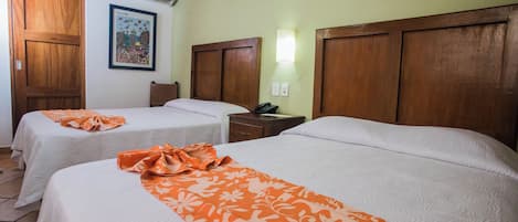 Dos camas con sábanas blancas y colchas florales naranja, cabeceros de madera, una mesita de noche con un teléfono, y un aplique de pared.