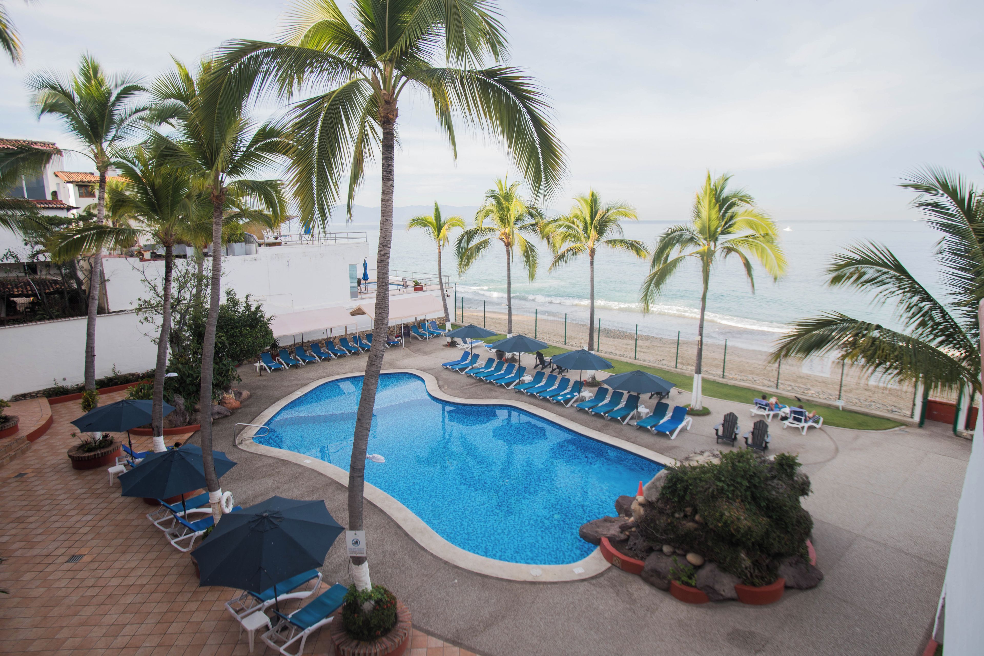 A pool area with lounge chairs and umbrellas, surrounded by palm trees and a view of the beach.