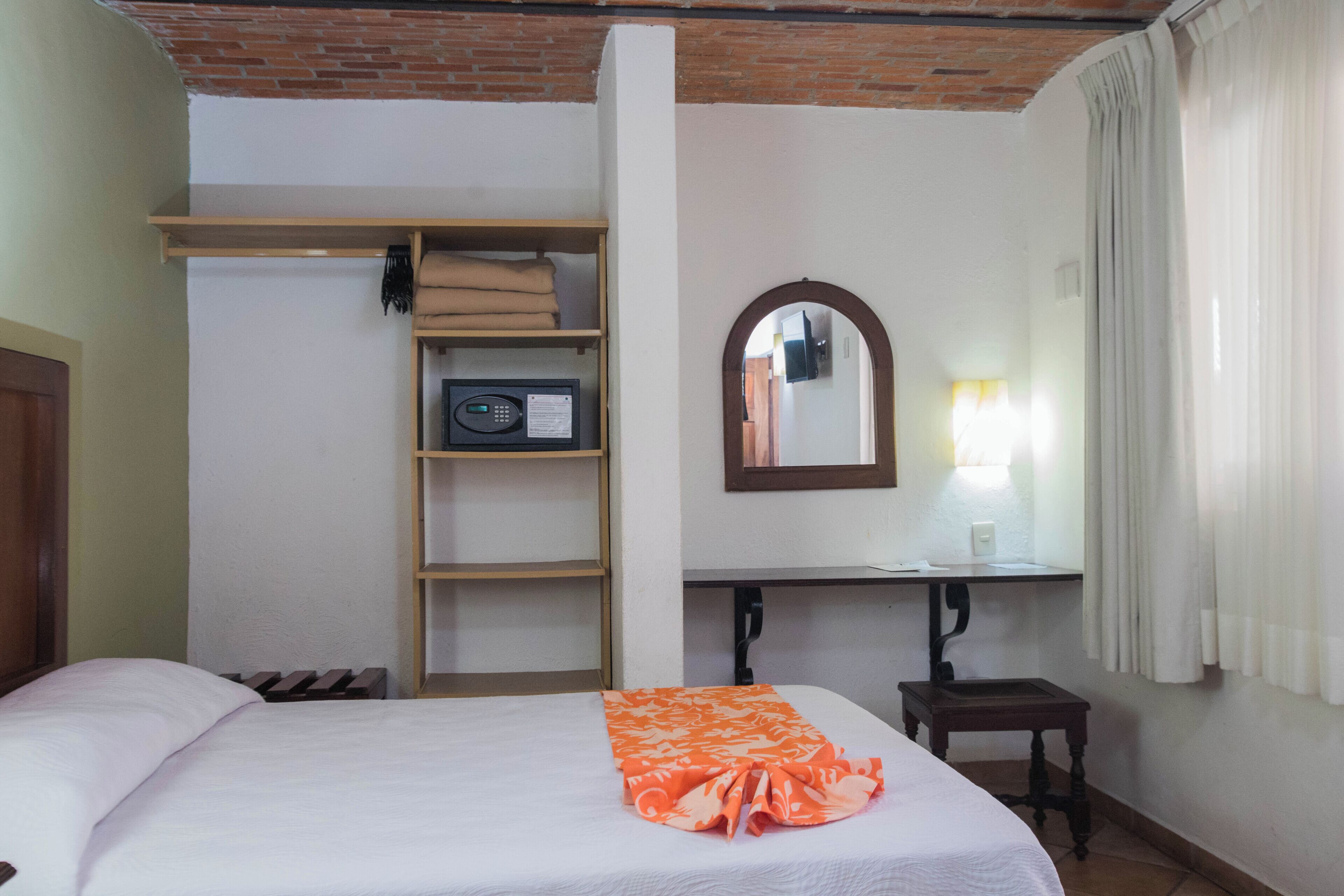 Una habitación de hotel con cama, armario, escritorio con espejo y una mesita.