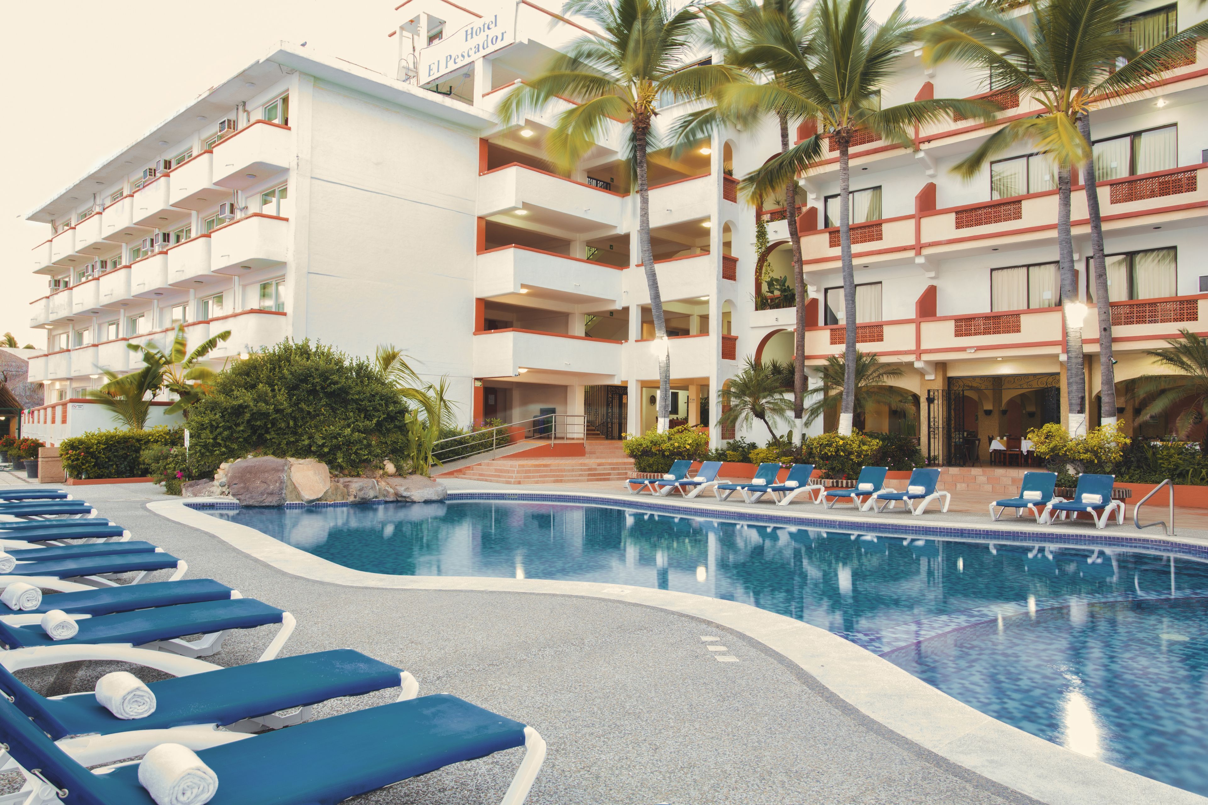 A hotel with a swimming pool, lounge chairs, and palm trees.