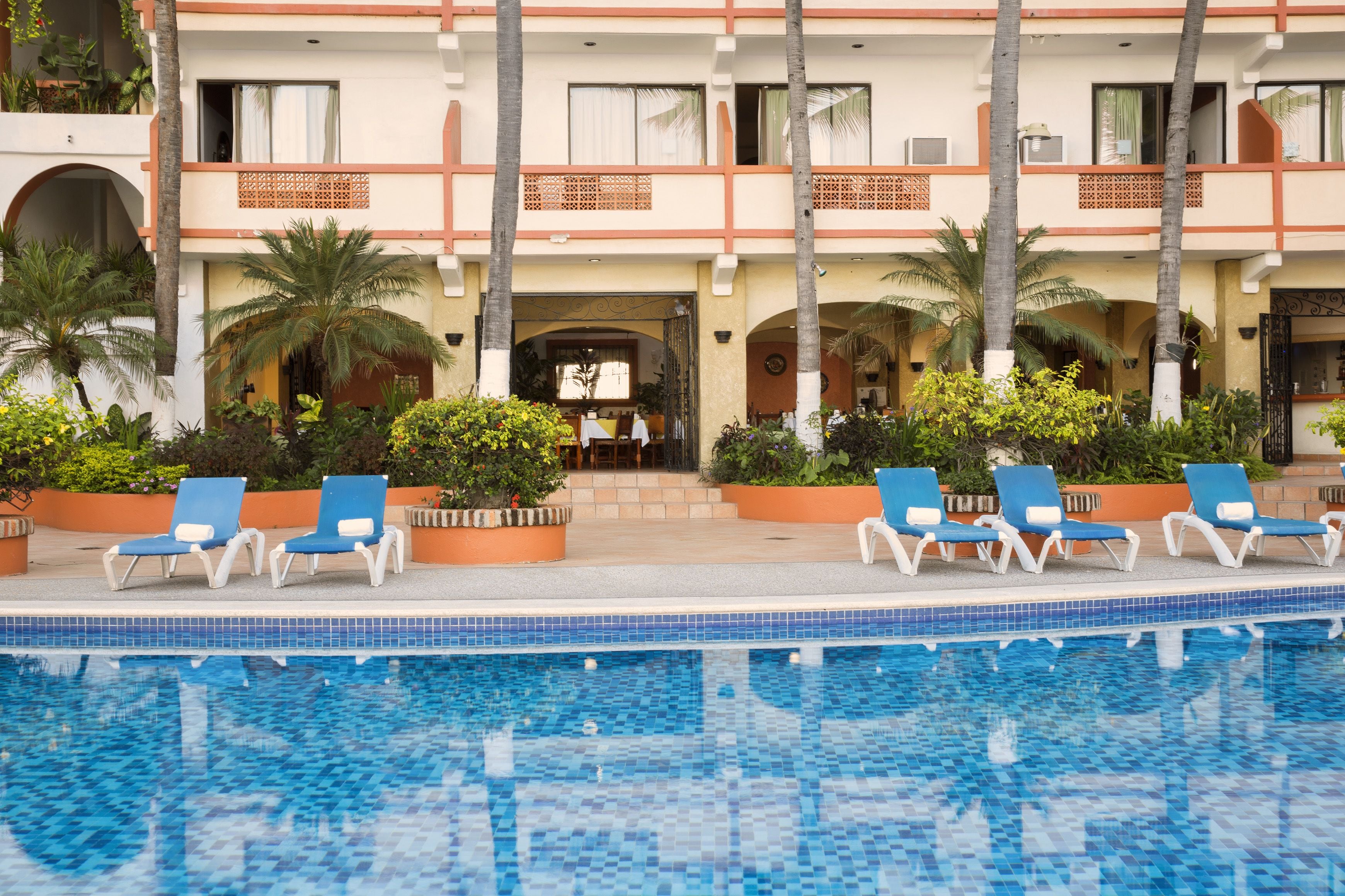 A hotel with a pool area, lounge chairs, and palm trees.