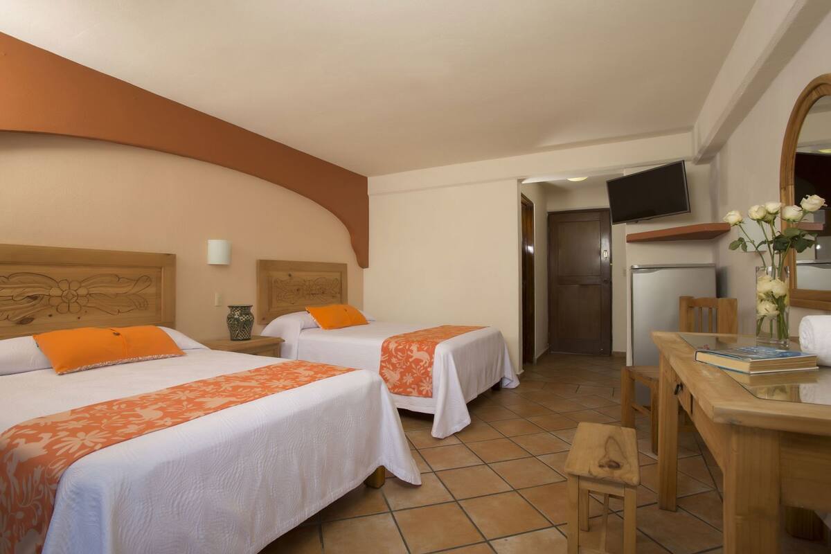 Habitación de hotel con dos camas, un escritorio, una silla, un televisor y una puerta.
