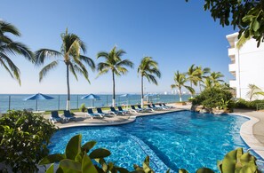 A pool area with lounge chairs and umbrellas, surrounded by palm trees and a view of the ocean. - El Pescador Hotel (Puerto Vallarta)