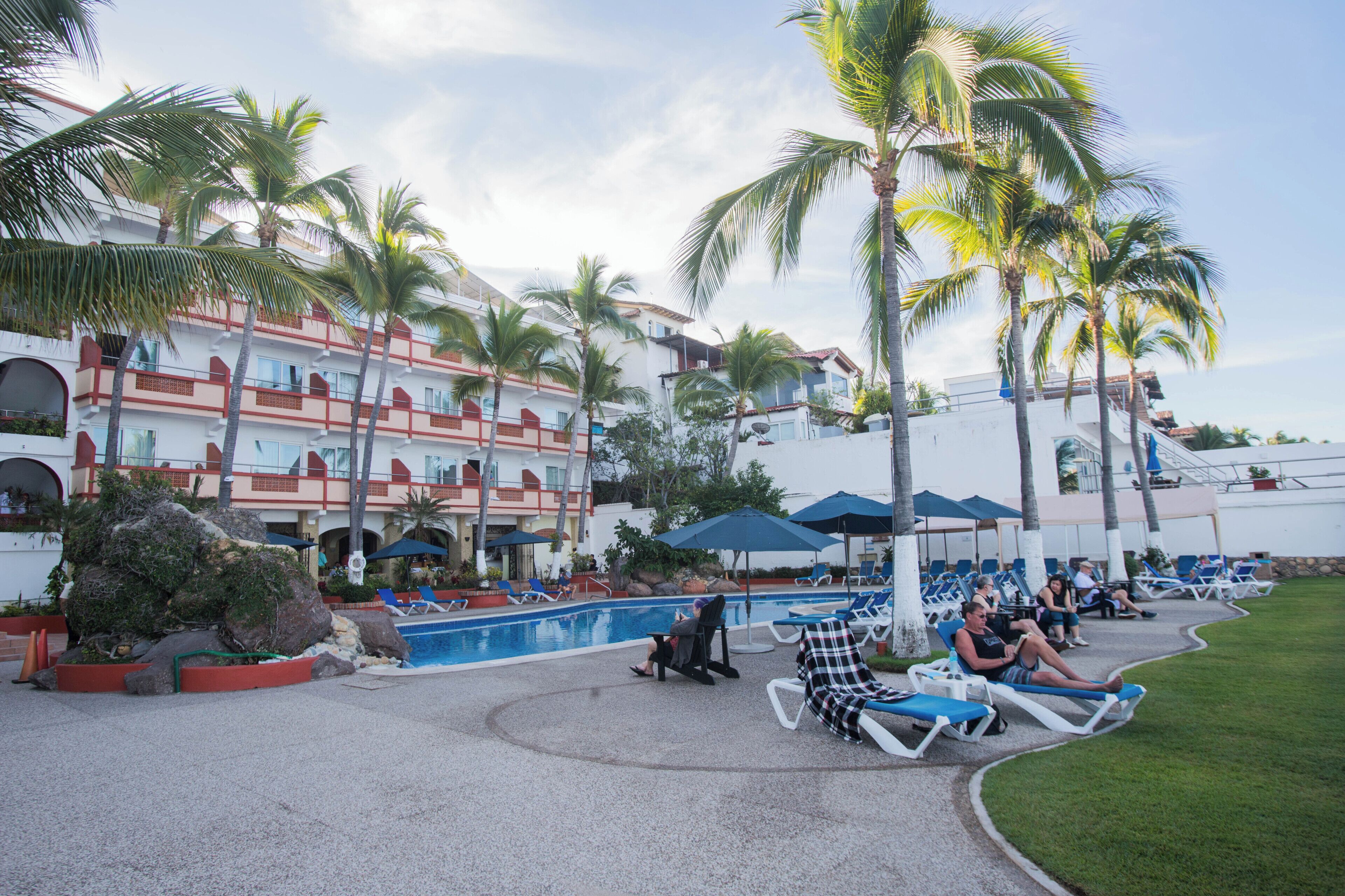 A resort with a pool area, palm trees, and lounge chairs.