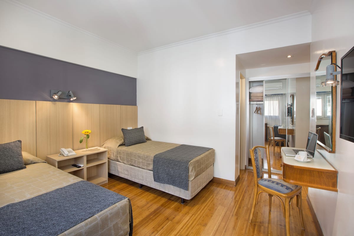 A hotel room with two beds, a desk with a laptop, a chair, and a small table with a phone.