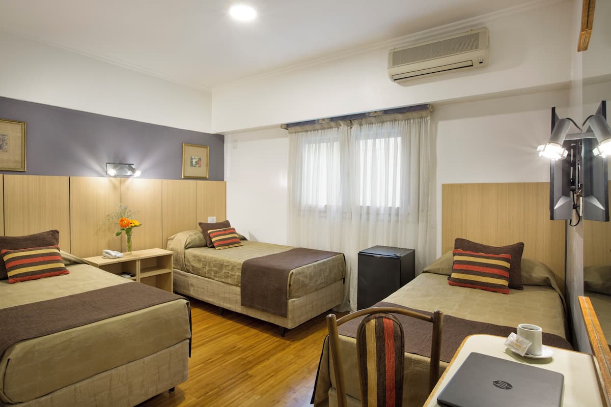 A hotel room with two single beds, a desk with a laptop, a chair, and a small table with a cup.