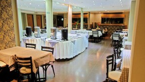 A spacious dining area with multiple tables and chairs, a buffet setup, and a large mirror on the wall. - Hotel Impala (Buenos Aires)