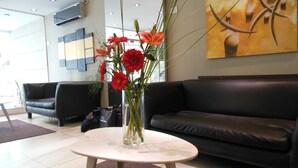 A modern lobby with a white table, a black leather sofa, and a vase with red flowers. - Hotel Impala (Buenos Aires)