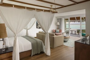 Relax in a spacious bedroom with a large bed under a canopy, a cozy seating area, and stunning ocean views through large windows.