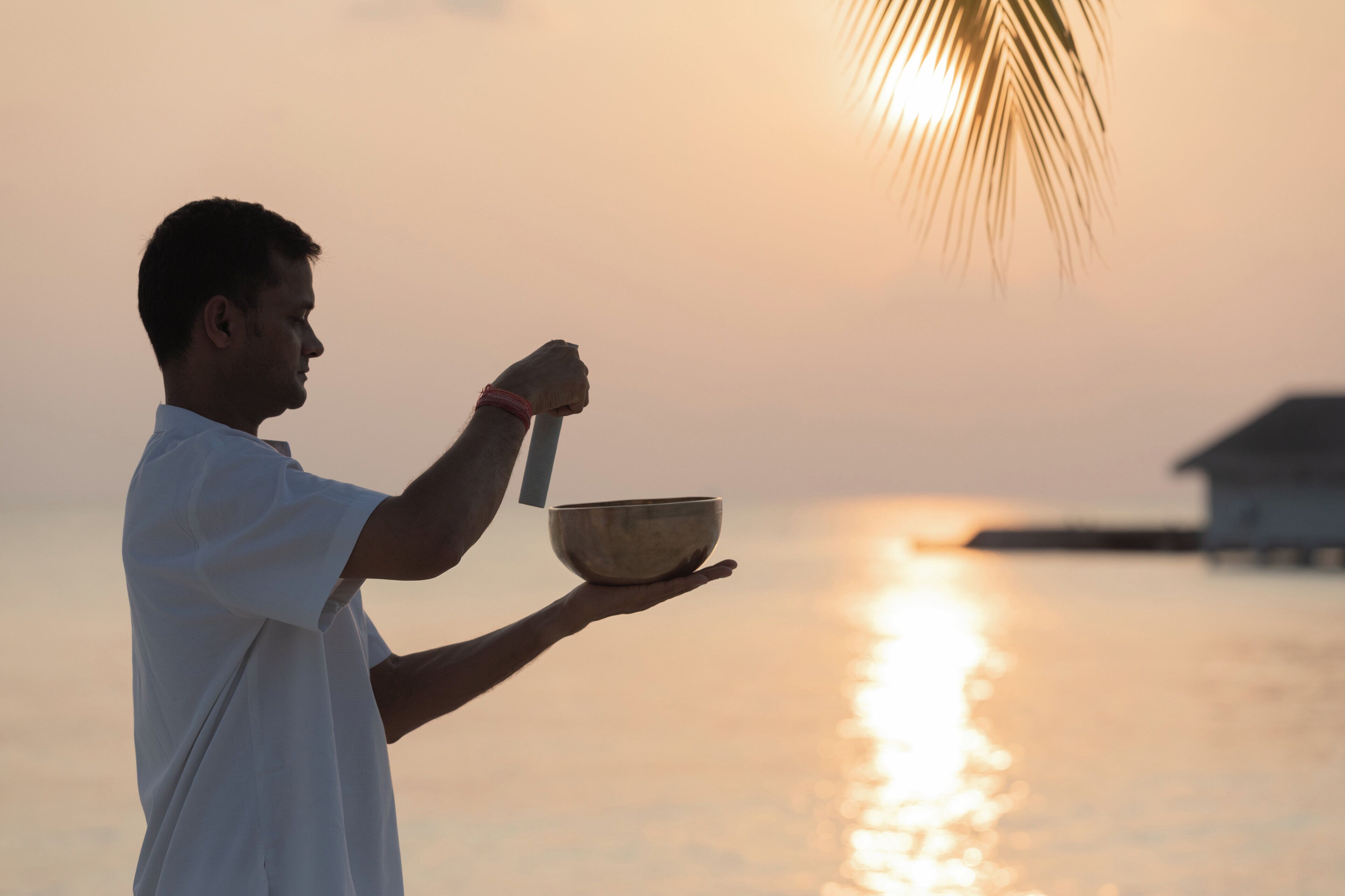 Una persona sosteniendo un tazón y una cuchara junto a un cuerpo de agua al atardecer.