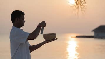 Una persona sosteniendo un tazón y una cuchara junto a un cuerpo de agua al atardecer.