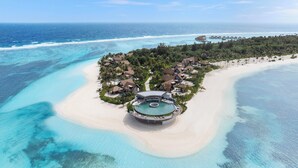 Luftaufnahme eines Resorts mit einem zentralen Pool, umgeben von Strand und Meer.