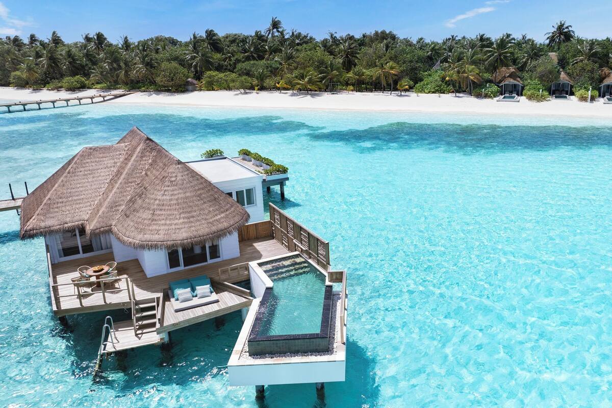 Ein überwasserbungalow mit Strohdach, privatem Pool und einer Terrasse.