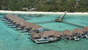 Wasserbungalows mit Strohdächern, verbunden durch Wege über türkisfarbenem Wasser.