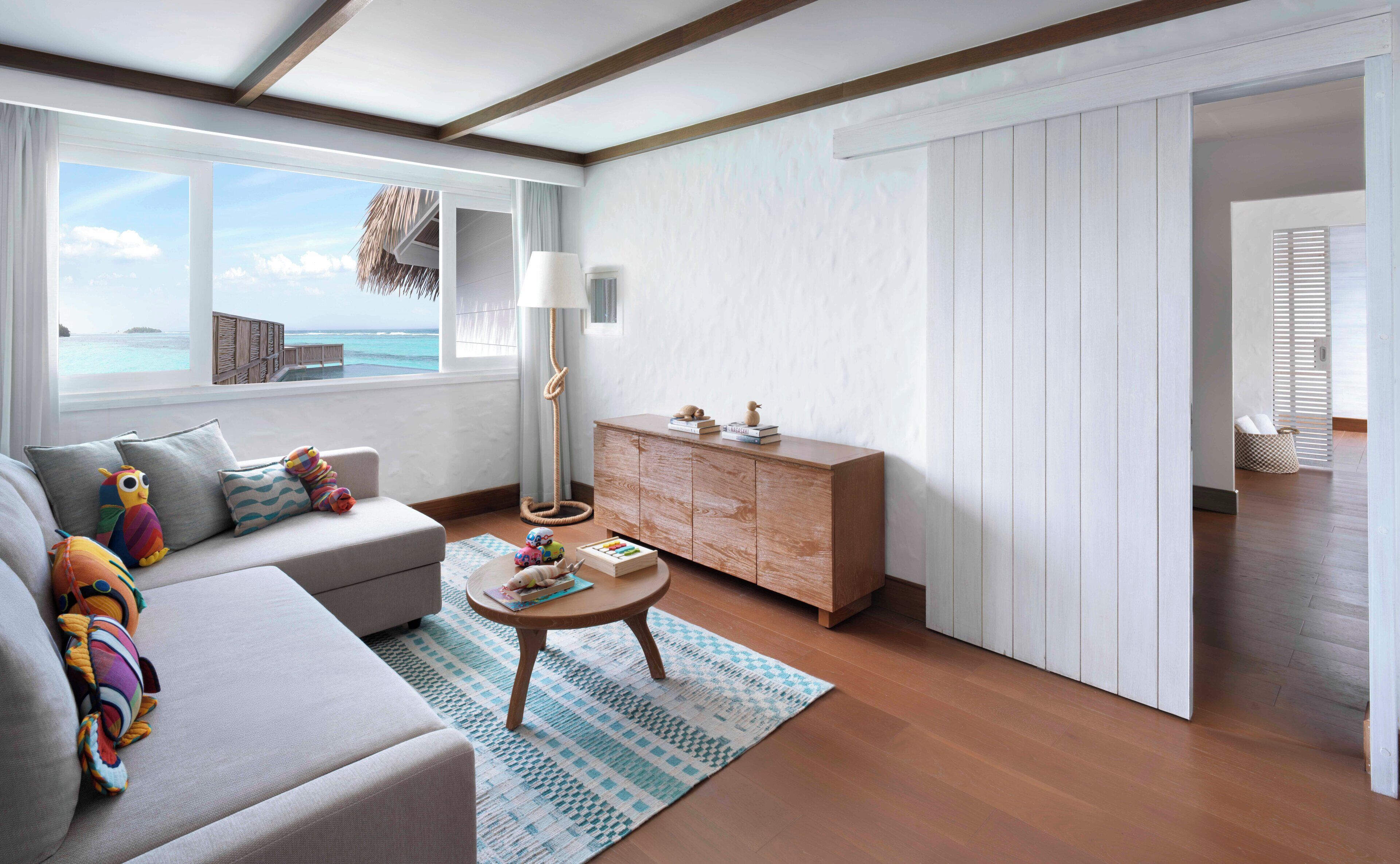 A modern living room with a sofa, a coffee table, and a wooden cabinet. There is a view of the ocean through large windows.