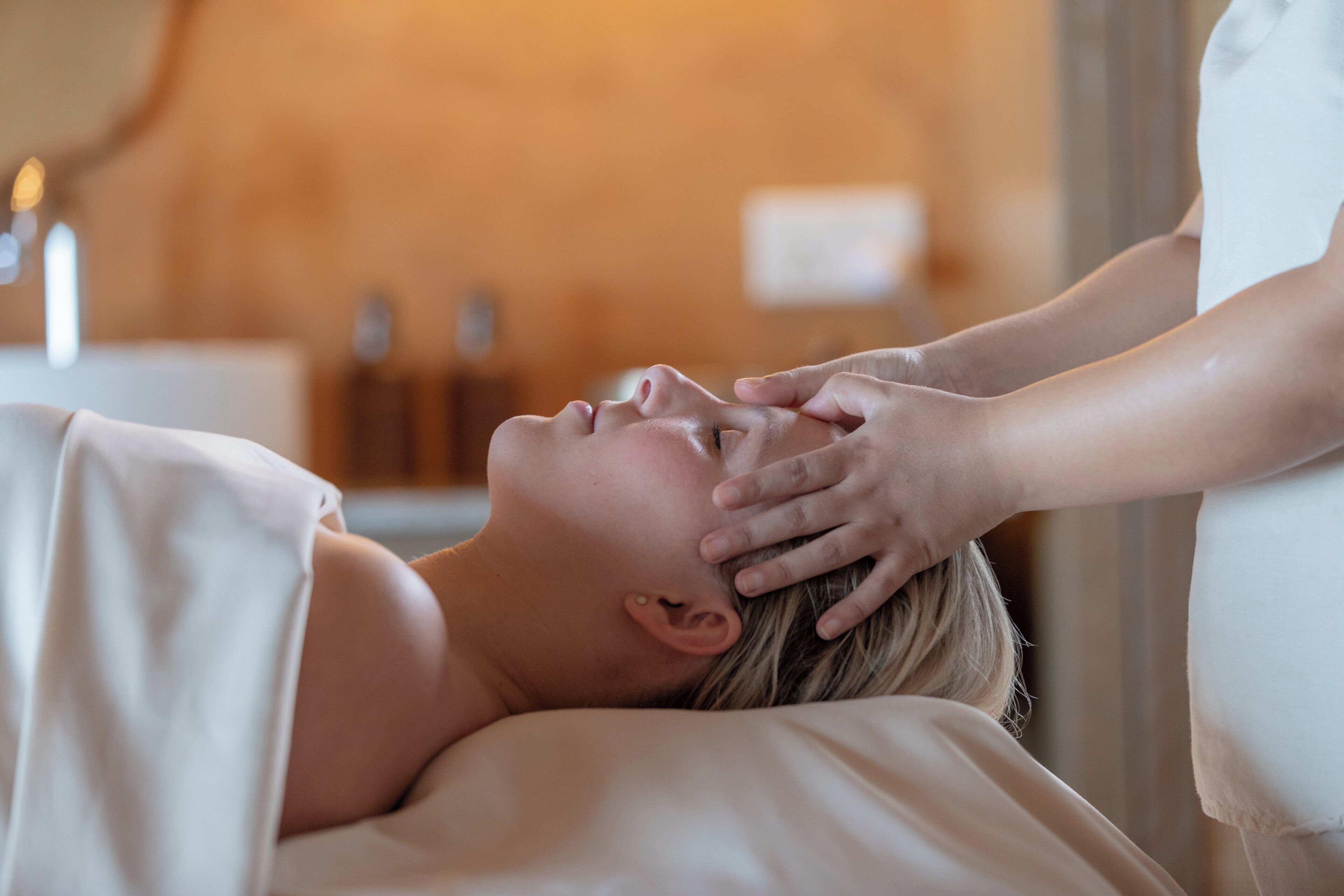 A person receiving a head massage in a room with a neutral color scheme and minimal decor.