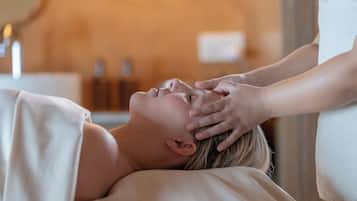 A person receiving a head massage in a room with a neutral color scheme and minimal decor.