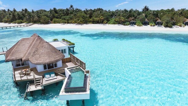 Ein Bungalow auf Stelzen über dem Wasser mit einem Reetdach, einem privaten Pool und Blick auf einen weißen Sandstrand und Palmen.