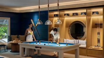 Une table de billard dans une pièce aux murs bleus, avec des meubles en bois et des luminaires suspendus.