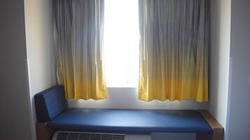 A small room with a bench, a window with curtains, and a wall-mounted air conditioning unit.