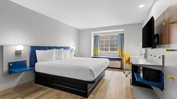 Habitació d'hotel moderna amb llit, televisió integrada i finestra amb cortines.