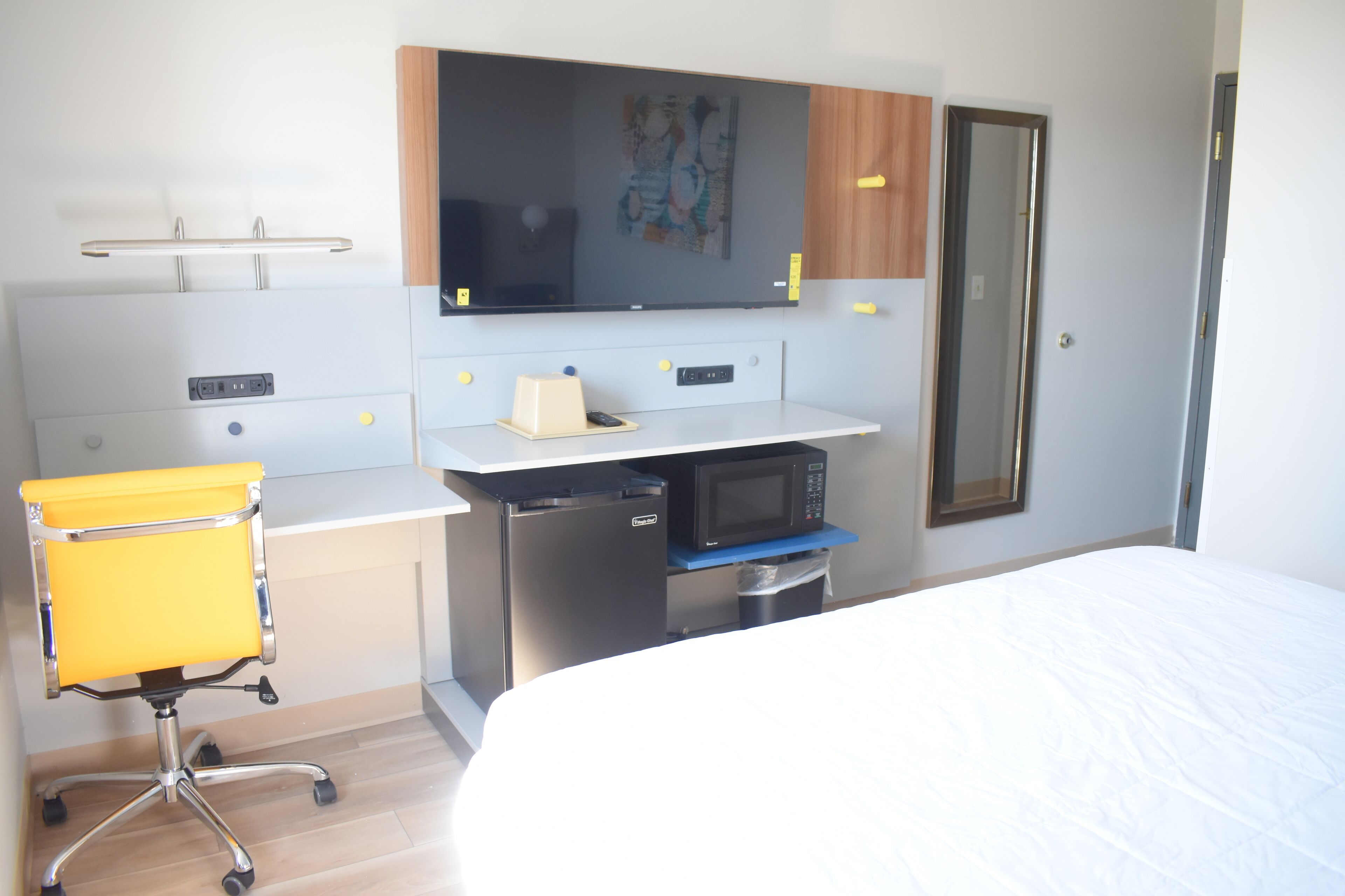 A hotel room with a bed, a desk with a microwave, a chair, and a small trash bin.