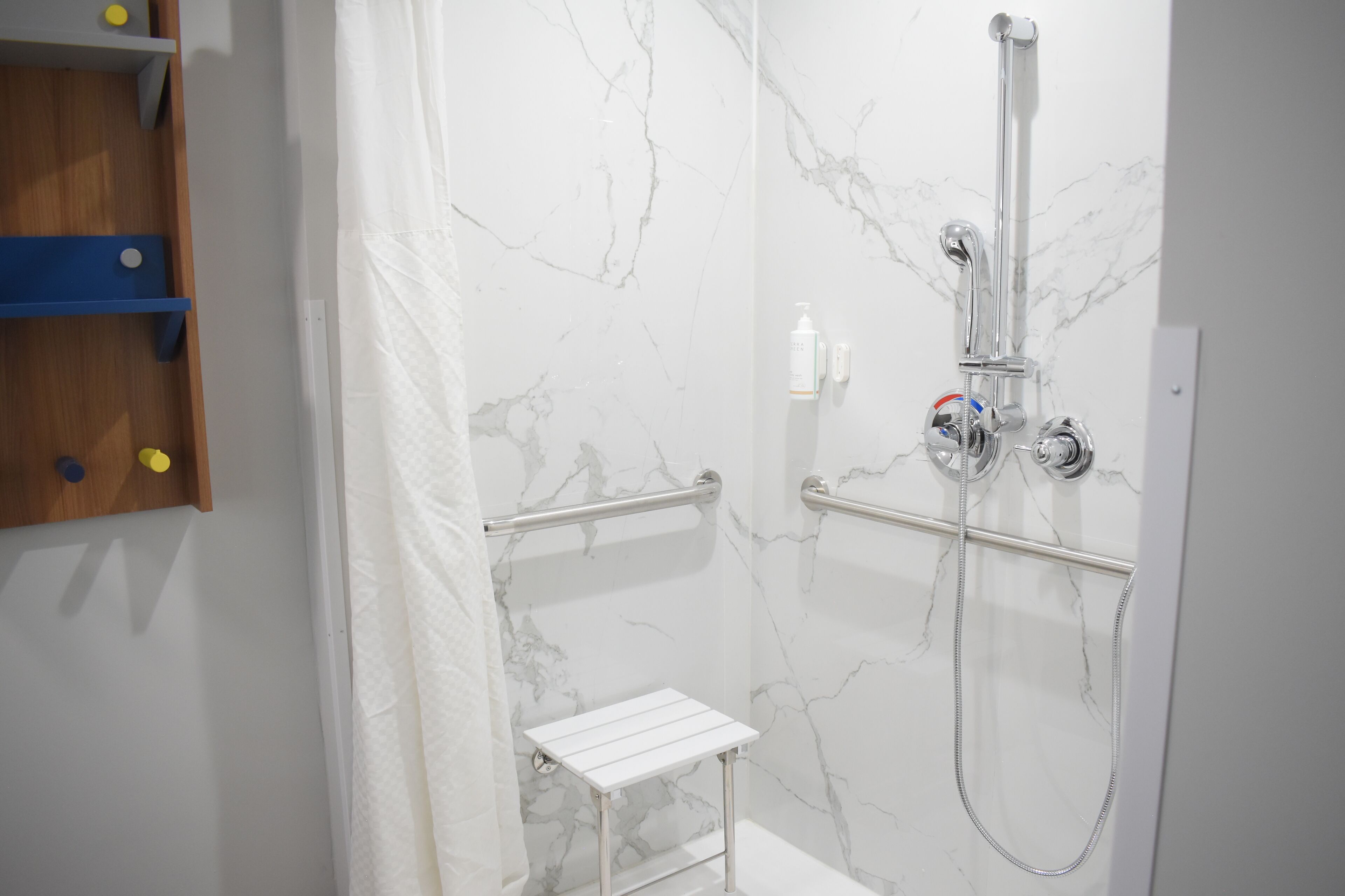 A modern bathroom with a shower, marble walls, and a small white shelf.