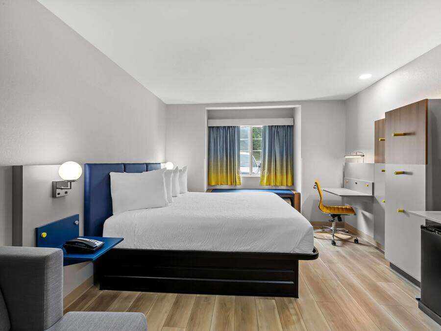 Una moderna camera d'albergo con un letto grande, una scrivania con lampada, una sedia, una TV e un frigorifero.