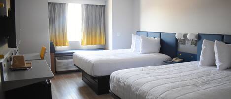 A hotel room with two beds, a desk, a chair, and a window with curtains.