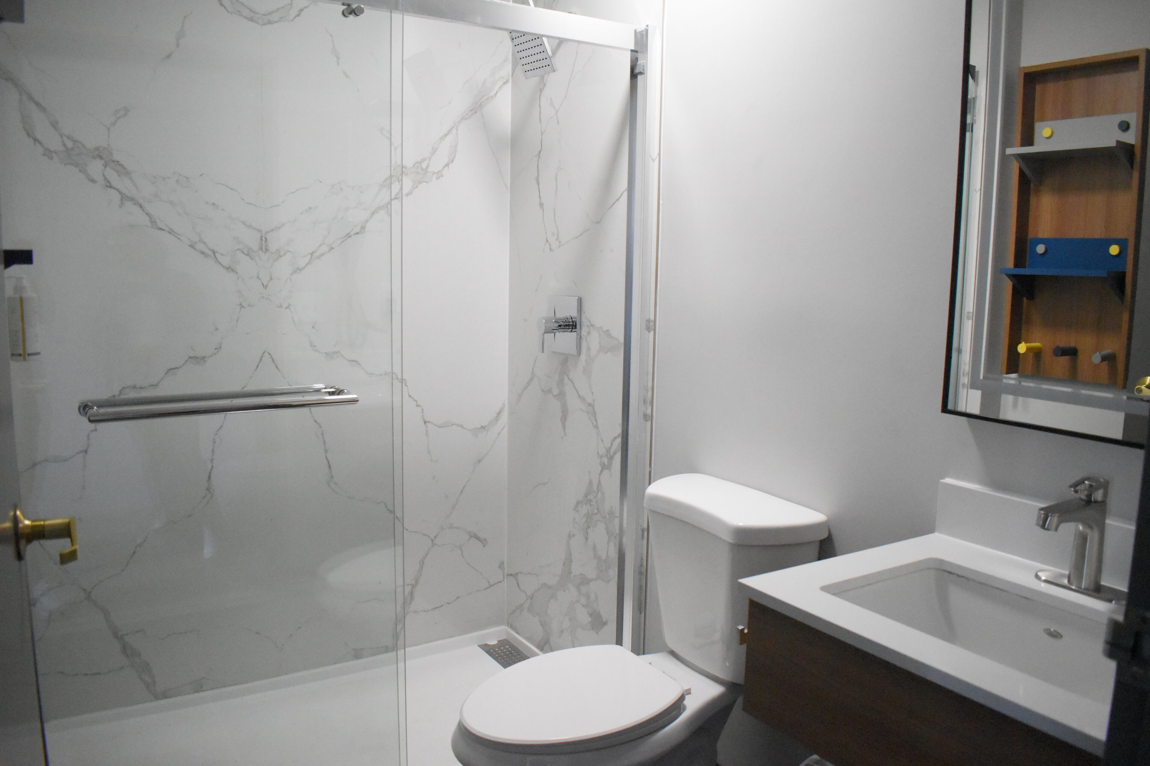 Un bany amb dutxa de vidre, un vàter blanc i un lavabo amb mirall a sobre.