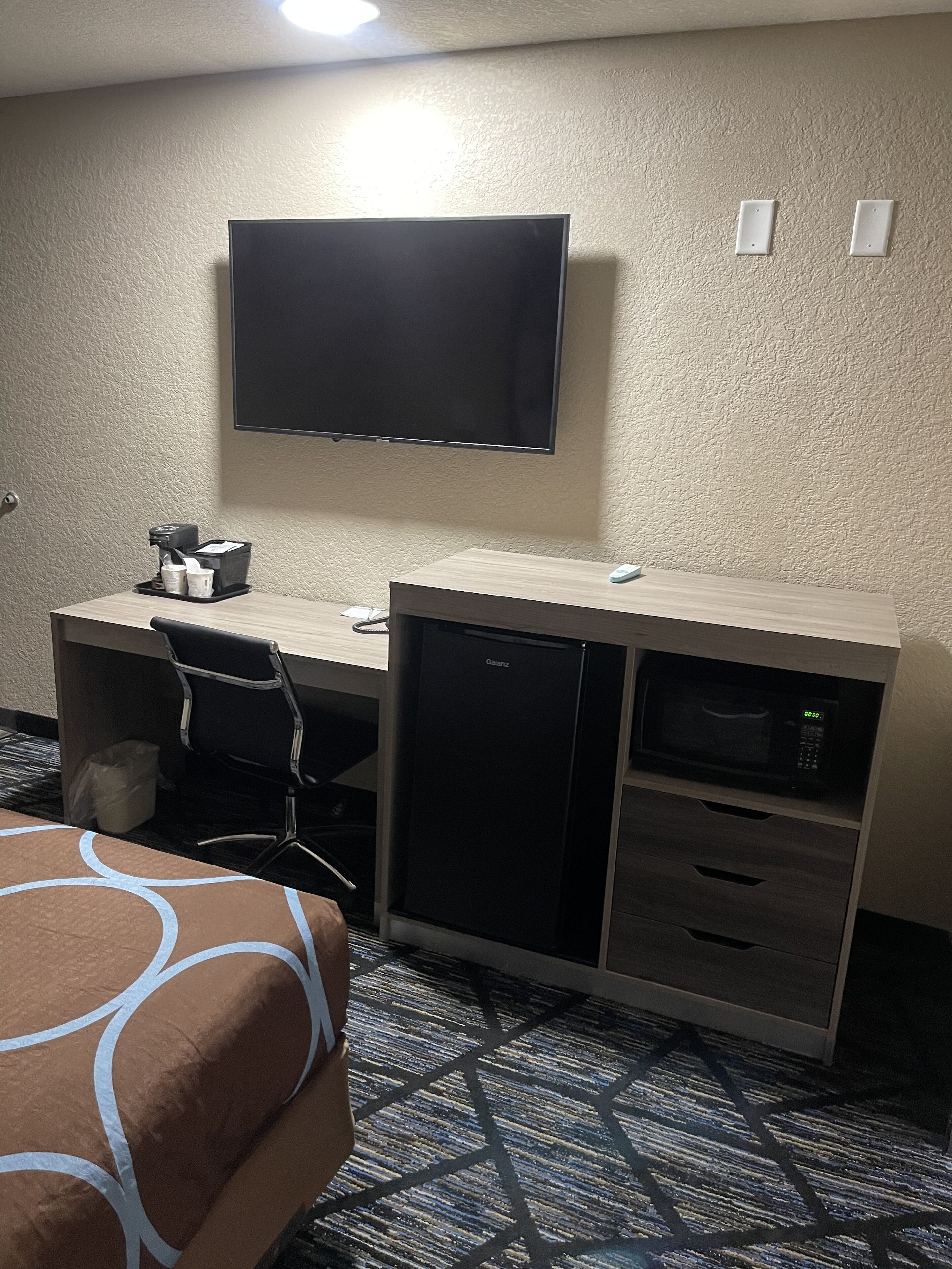 Habitación de hotel con cama, escritorio con televisor de pantalla plana, microondas y refrigerador pequeño.