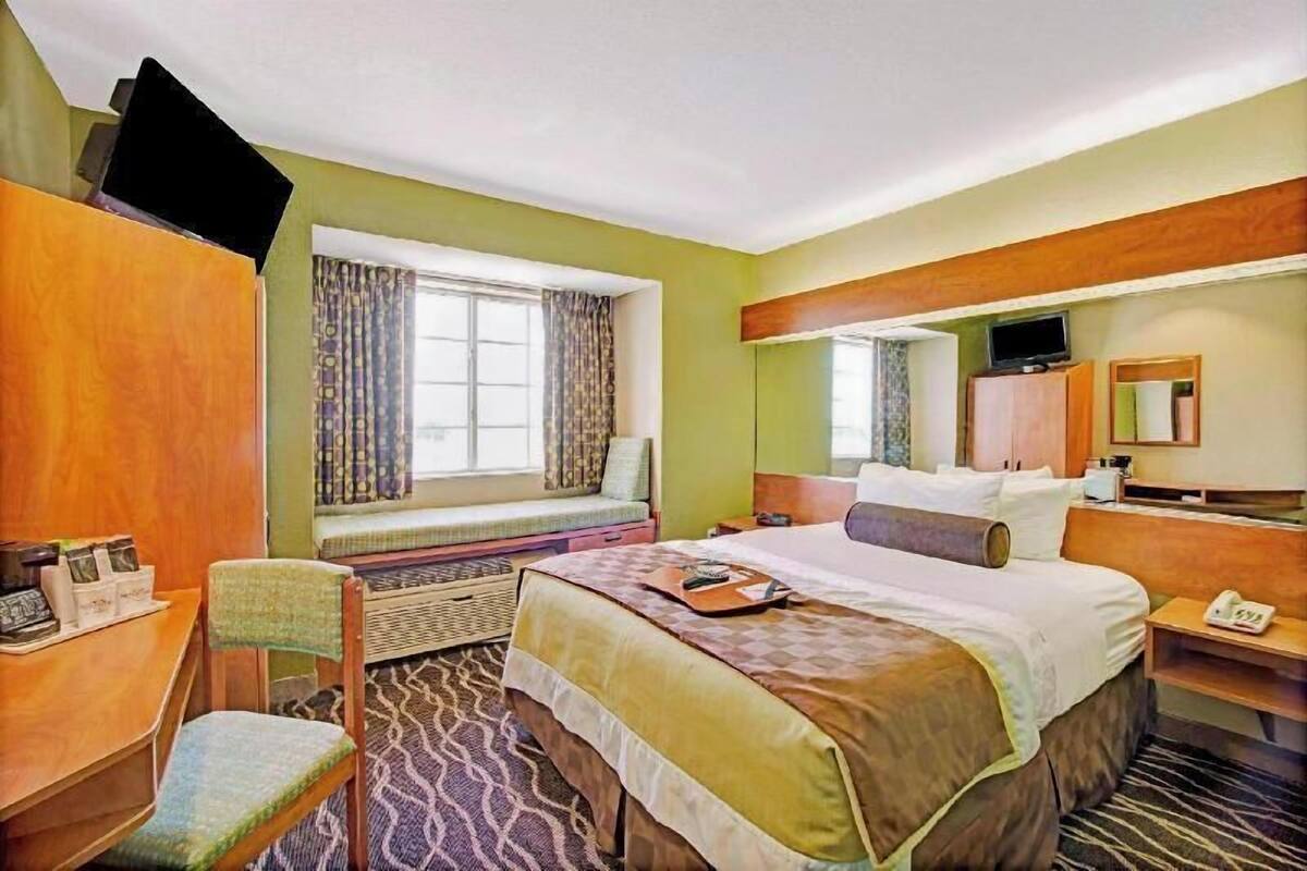 Una habitación de hotel con cama, escritorio, silla, televisor y ventana con cortinas.