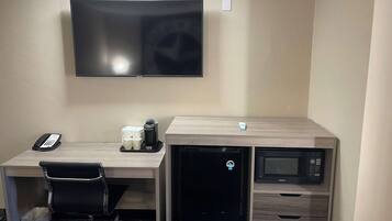 A hotel room with a flat-screen TV mounted on the wall, a desk with a chair, a coffee maker, a mini-fridge, and a microwave.
