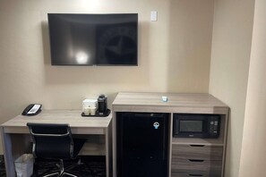 Une chambre d’hôtel équipée d’un téléviseur à écran plat fixé au mur, d’un bureau avec une chaise, d’une machine à café, d’un mini-réfrigérateur et d’un four à micro-ondes.