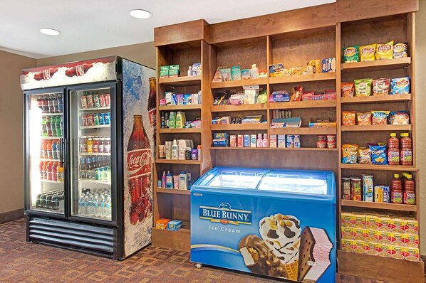 Una zona de máquinas expendedoras con un refrigerador de Coca-Cola, un congelador de helados Blue Bunny y estantes llenos de aperitivos y bebidas.