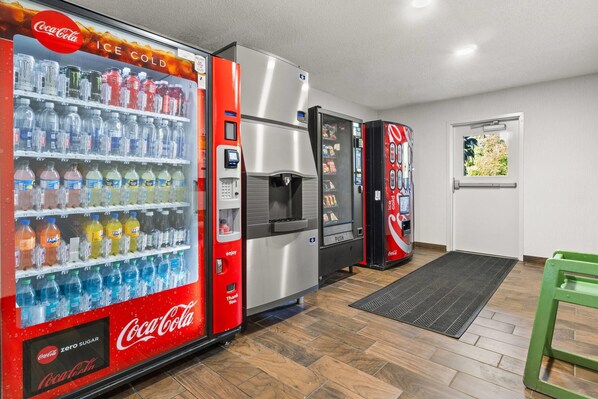 A vending area with Coca-Cola and other beverage machines, a refrigerator, and a door with a window view.