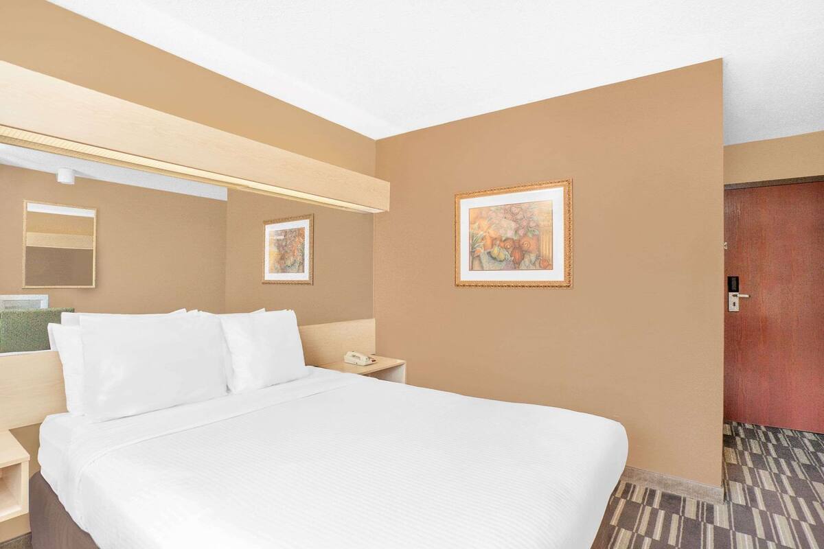 A hotel room with a large bed, a bedside table, a nightstand, a mirror, and two framed pictures on the wall.