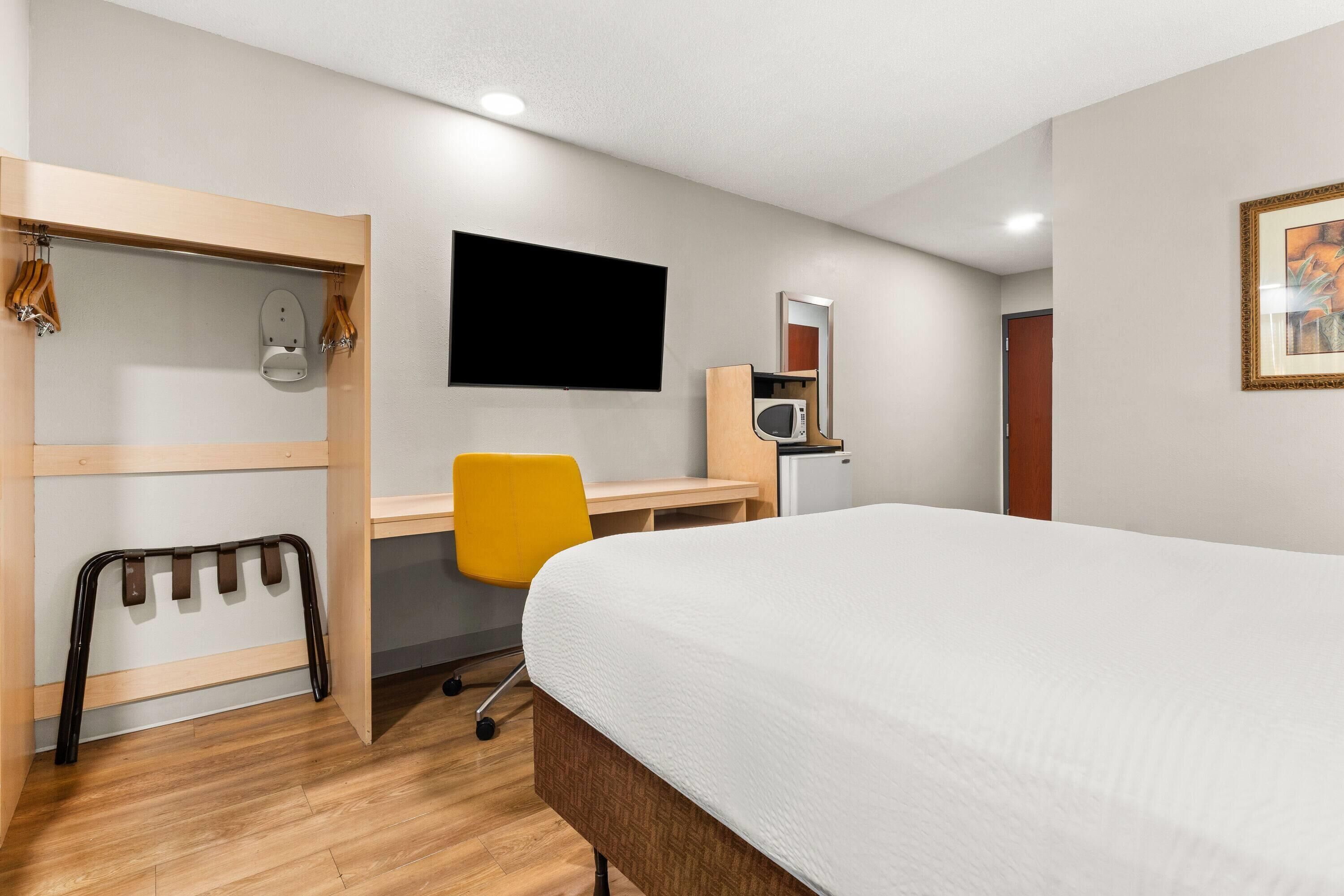 A hotel room with a bed, a desk, a chair, a TV, a microwave, and a wardrobe.