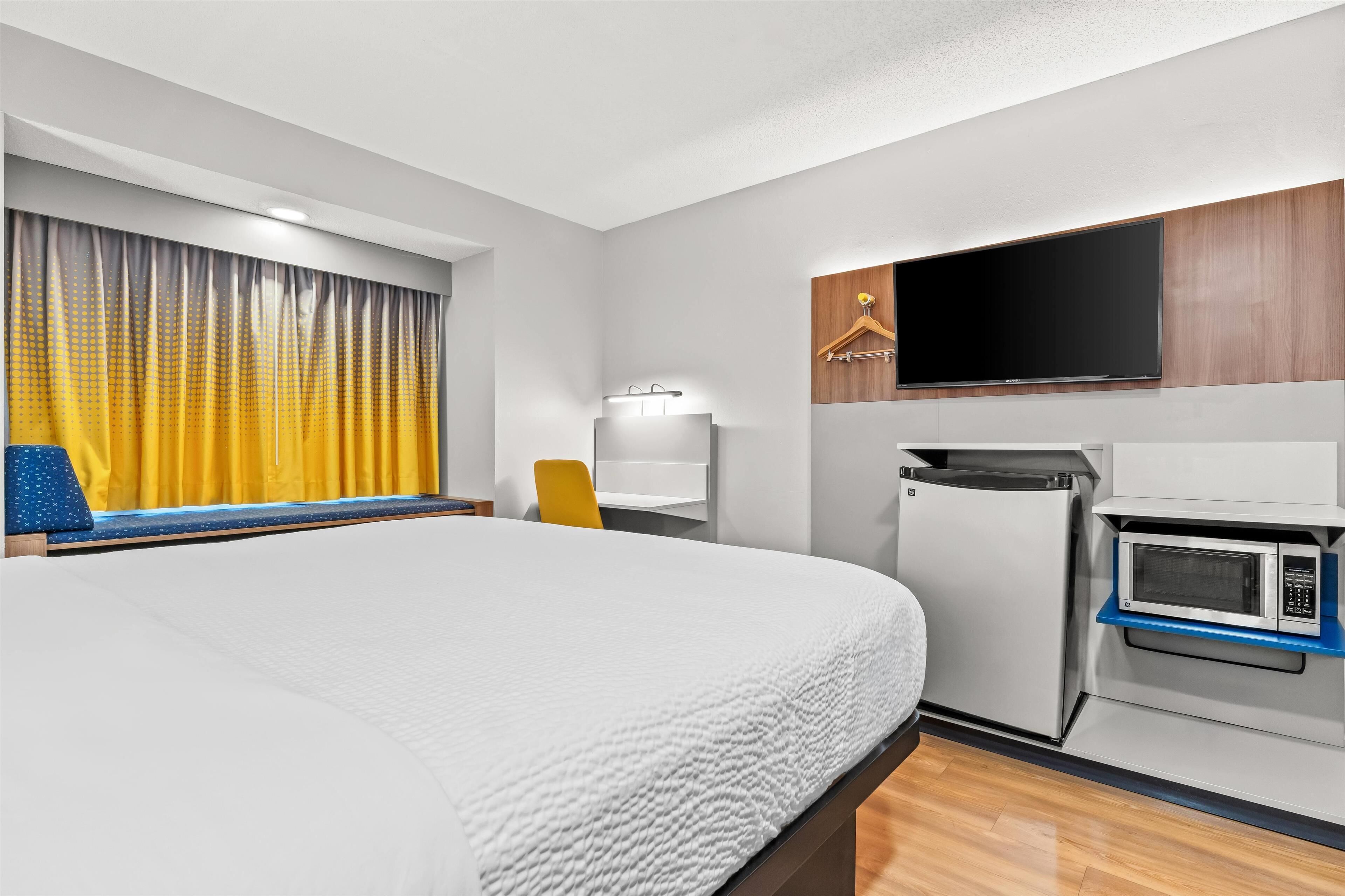 A hotel room with a large bed, a flat-screen TV mounted on the wall, a microwave, and a small refrigerator.