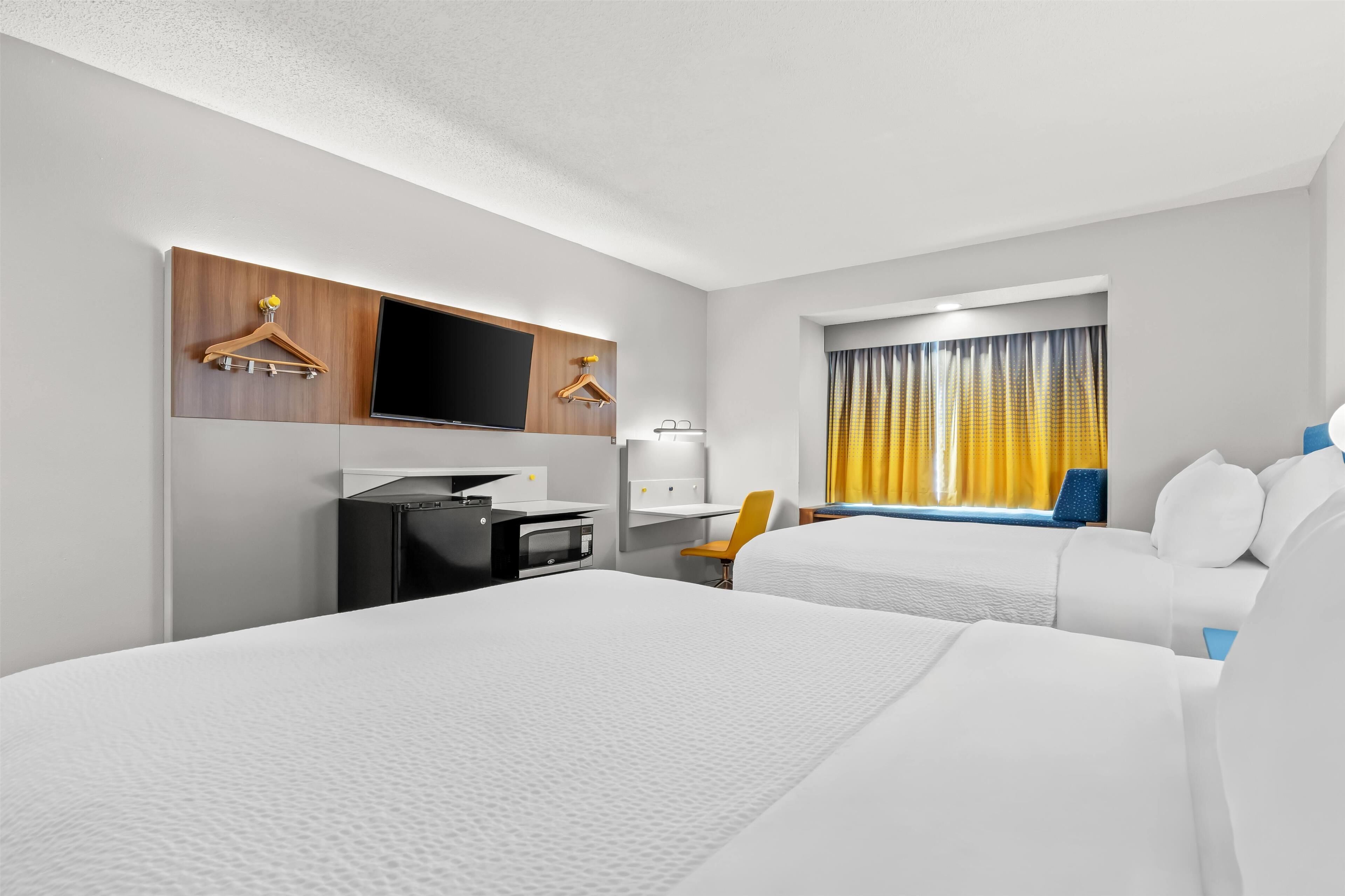 A hotel room with two beds, a desk, a TV, and a window with curtains.
