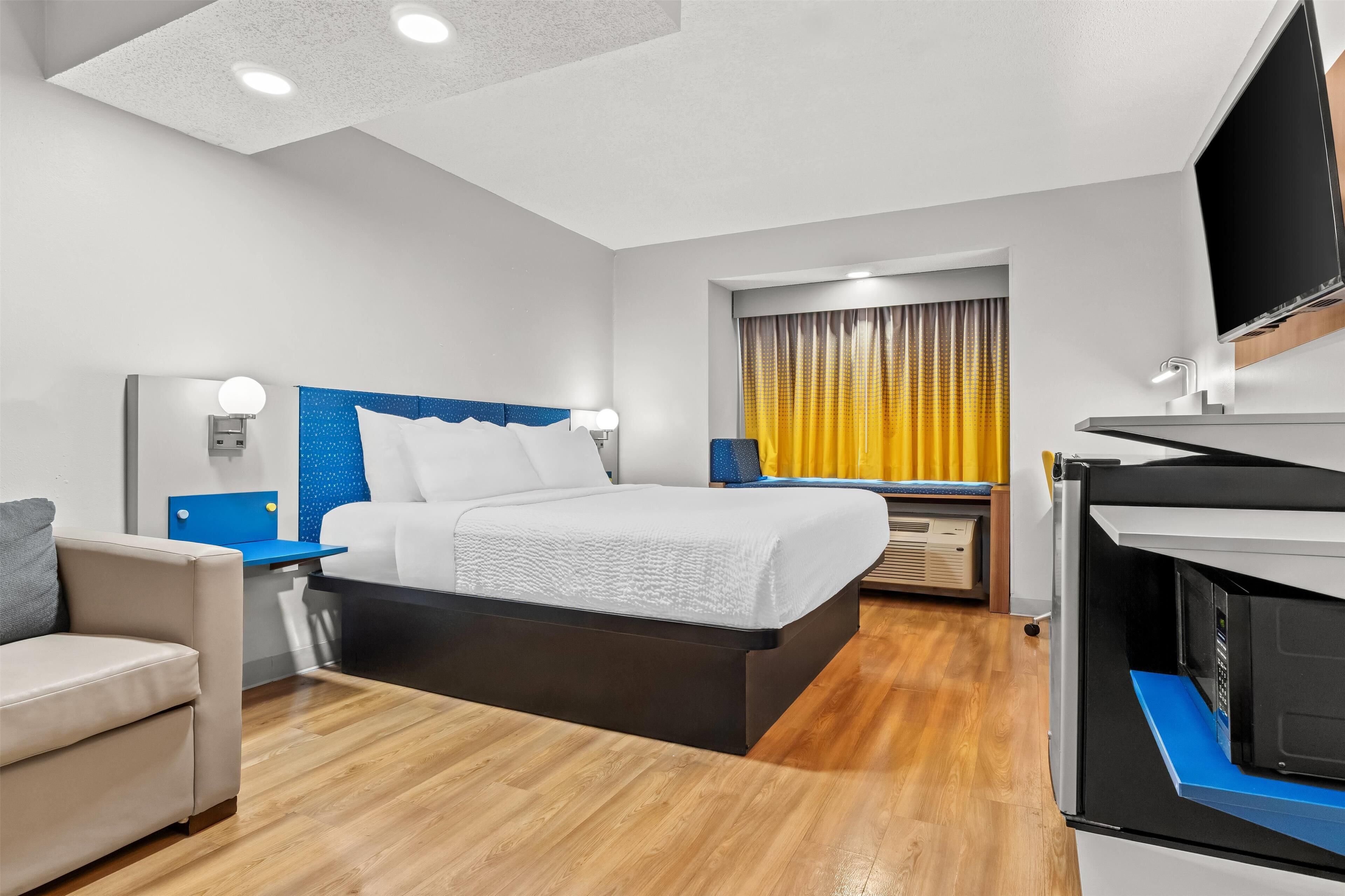A modern hotel room with a large bed, a desk, a TV, and a bathroom with a shower and toilet.