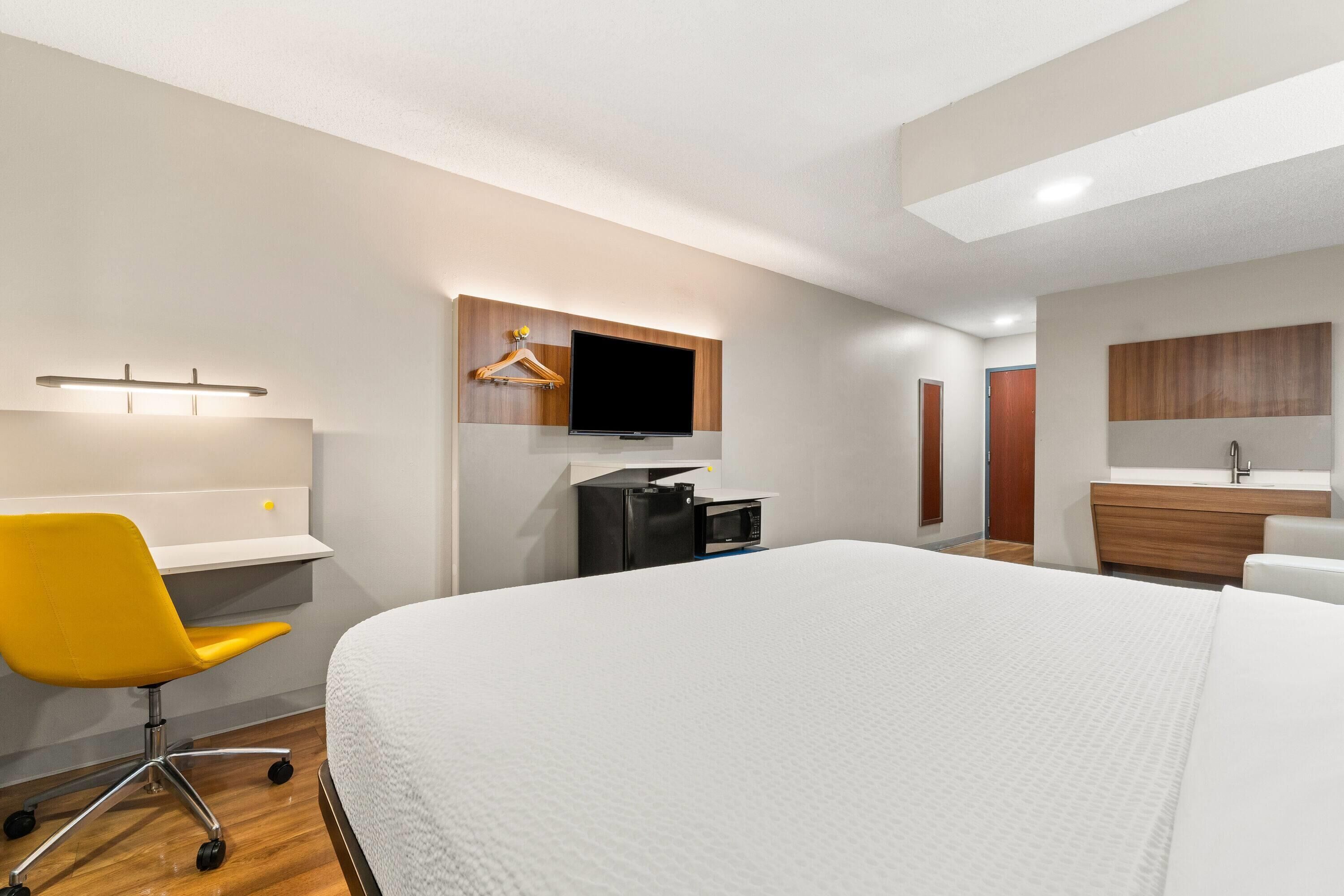 Una habitación de hotel moderna con una cama grande, un escritorio con silla, un televisor, un armario y un baño.