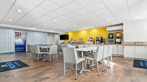 A modern dining area with a yellow accent wall, a kitchen area with appliances, and a large screen.
