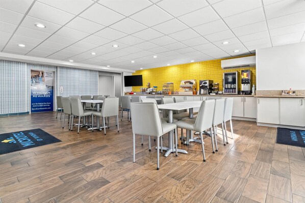 A modern dining area with a long table and chairs, a kitchen area with a yellow backsplash, and a refrigerator.