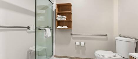 A modern bathroom with a glass shower enclosure, a toilet, and a wooden shelf with towels.