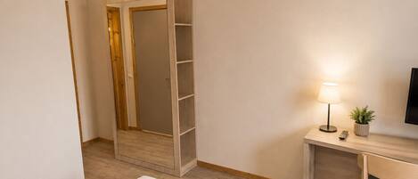 A hotel room with a bed, a desk with a lamp, a TV, and a wardrobe.