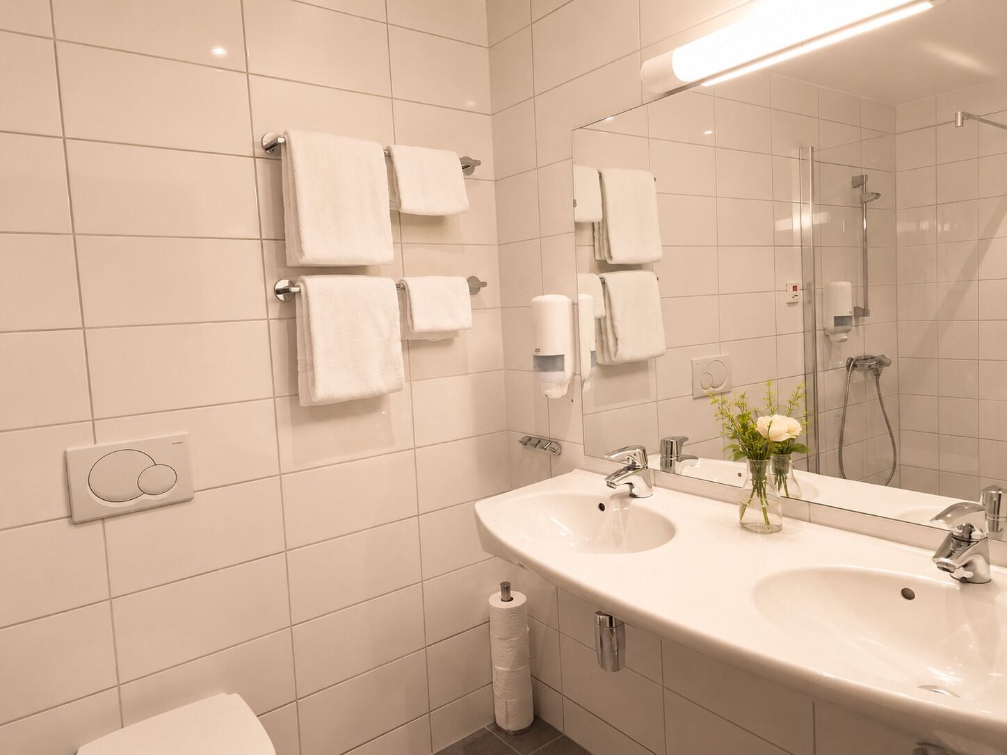A modern bathroom with a large sink, mirror, and multiple towel dispensers.