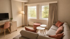 A modern living room with a sofa, a TV, a lamp, a small table, and a view of greenery outside. - Haukeland Hotell (Bergen)