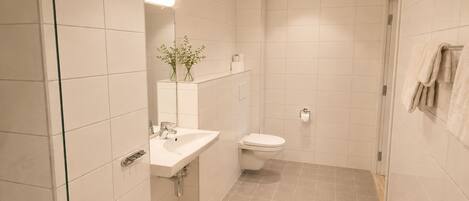 Un baño moderno con lavamanos, inodoro y zona de ducha blancos.