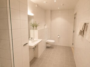 Un baño moderno con lavamanos, inodoro y zona de ducha blancos.